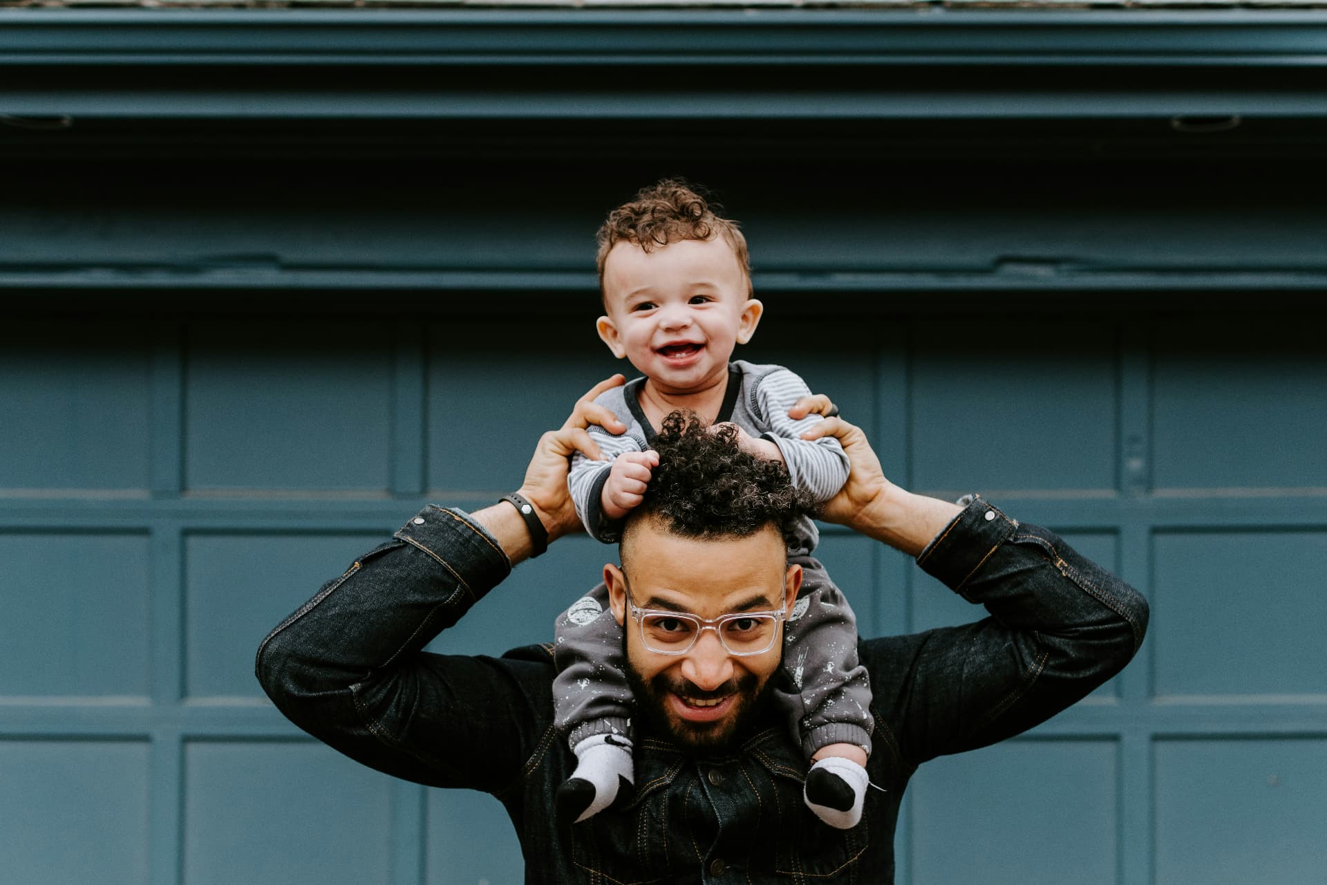A father lifting his laughing toddler onto his shoulders outdoors