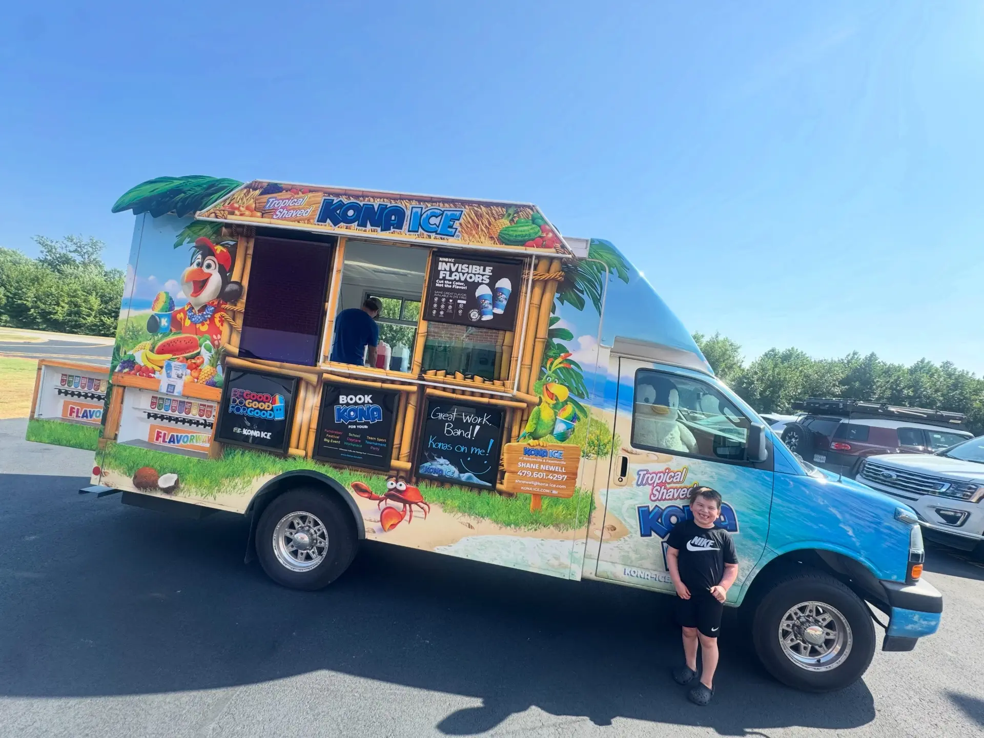The Kona Ice truck parked outside Siloam Springs High School with a student smiling in front of it