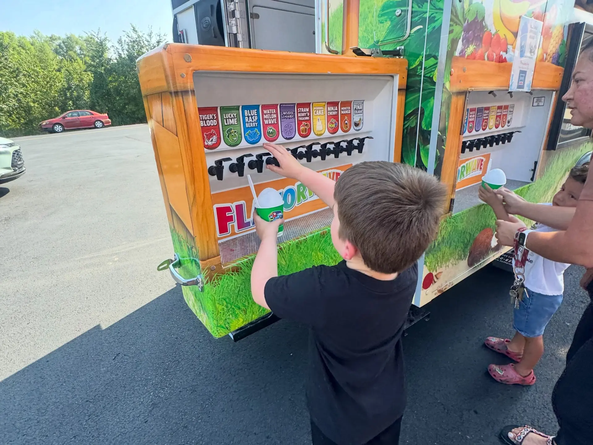 A child adding syrup from the Kona Ice flavor wave station to a cup of shaved ice